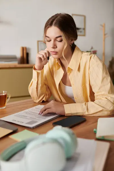 Молодая женщина сидит за деревянным столом, глубоко сосредоточенная на рассмотрении своих заметок. — стоковое фото