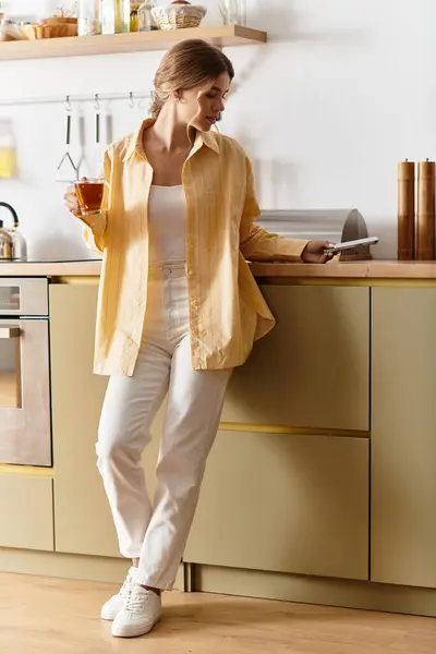 Una bella giovane donna si rilassa a casa in una cucina illuminata dal sole, assaporando il suo tè e momenti di pace. — Foto stock