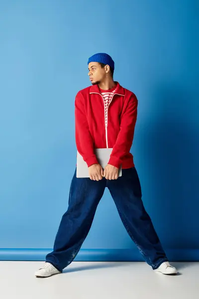 Un elegante giovane uomo nero in un berretto posa con fiducia su uno sfondo blu brillante. — Foto stock