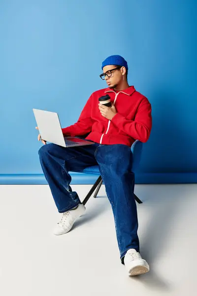Um jovem americano africano na moda em um gorro azul gosta de café enquanto trabalha intensamente. — Fotografia de Stock