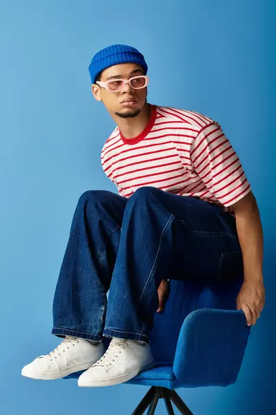 Un giovane alla moda che indossa un berretto siede con stile su una sedia, mostrando il suo senso della moda unico.. — Foto stock