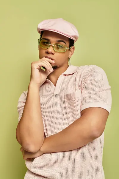 Un joven afroamericano de moda posa con confianza usando una camisa de polo rosa y una gorra plana. - foto de stock