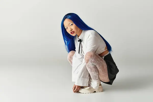 Молодая женщина с голубыми волосами стильно позирует в серой студии, демонстрируя свой модный наряд. — стоковое фото