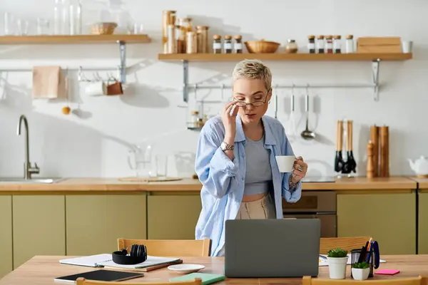 A young woman with short hair sips coffee, focused on her laptop in a stylish kitchen. — Stock Photo