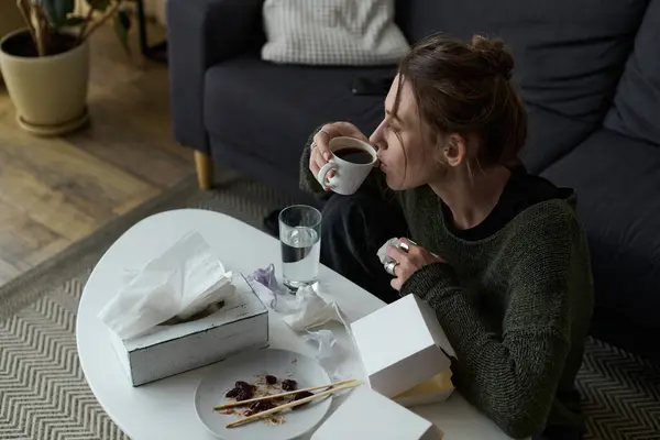 Молодая женщина сидит одна дома с чашкой кофе, чувствуя себя подавленной и интроспективной. — стоковое фото