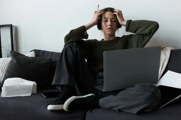 Woman experiences sadness and stress at home, seated on a couch with headphones on. — Stock Photo