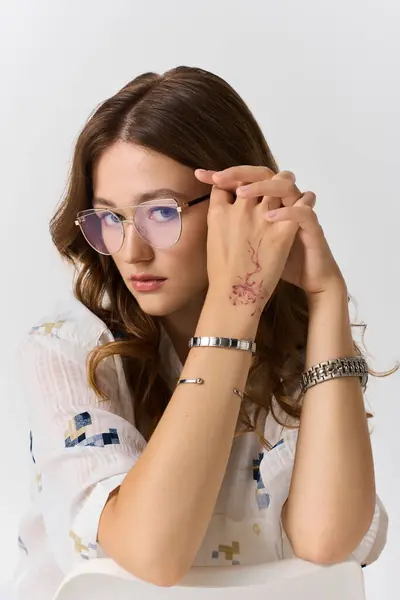 Jeune femme à la mode met en valeur son style avec des lunettes et un tatouage magnifique sur son bras. — Photo de stock