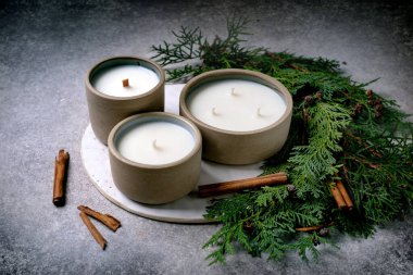 Seramik kaplarda üç farklı boyutta el yapımı aromatik mum. Eşkıya dalları ve tarçın çubuklarından yapılmış bir dekor. Noel havası. Noel hediyeleri. Gri desenli arka plan