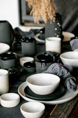 Boş el yapımı seramik sofra takımı, siyah ve beyaz kaba kaseler, kupalar, sürahi ve keten masa örtüsü üzerine vazo. Kuru kamış çiçekleri. Gün ışığı yemek odası.
