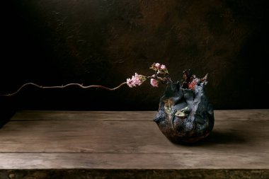 Bahar minimalist ikebana. Bahar çiçekleri açan çiçekli çiçek kompozisyonu, siyah seramik vazoda siyah tahta masada duran yusufçuk çiçekli kuru bir dal. Japon tarzı ev dekorasyonu