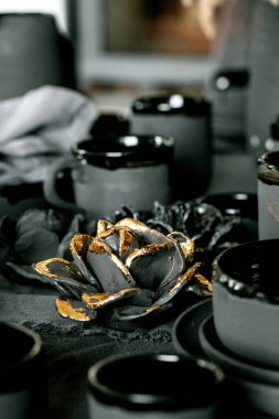 Boş el yapımı seramik sofra takımı, siyah kâseler, tabaklar, bardaklar, sürahi ve vazo ve keten masa örtüsü. Kırpılmış seramik güller çiçek dekoru. Gün ışığı yemek odası.