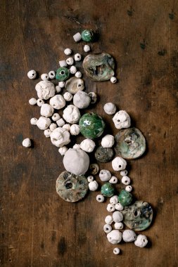 Çeşitli şekiller ve renkler el yapımı seramik boncuklar, jöleli ve parlatılmamış. Hobi, mücevher montajı, mücevher. Atölye fikri. Koyu ahşap arkaplan, üst manzara.