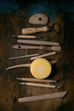Kil işleme aletleri seti. Çamur ögelerini budamak ve şekillendirmek için eski çömlek araçları, tel aracı, kesme ipi, eskimiş ahşap masa üzerinde sünger koyu arkaplan.
