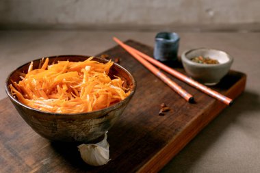 Dish of Korean and Asian cuisine: vegetable salad marinated carrots with garlic. Served in ceramic bowl with chopsticks. Seasoning in small bowls on Mocha Mousse tones table. Healthy eating. Close-up clipart