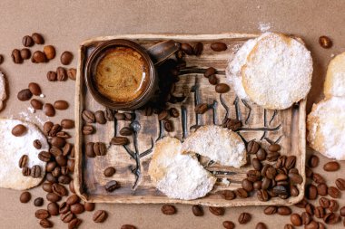 Toz şekere bulanmış ev yapımı kurabiye. Köy tatlısı, ev yapımı hamur işi. Seramik tepside kahve çekirdekli bir fincan espresso. Arka plan 2025 Yılın Rengi, Mocha Mousse. Üst görünüm.