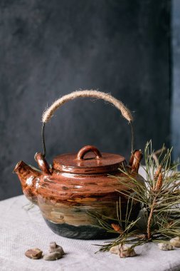 Geleneksel çay için el yapımı seramik çaydanlık masa örtüsü ile birlikte masada içiliyor. Dekoratif deniz taşları ve ladin dalları her yerde. Arka plan olarak karanlık duvar. Boşluğu kopyala