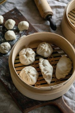 Making Asian steamed dumplings with vegetable filling. Dumplings ready to cook in bamboo steamer, ingredients nearby, floured board. Natural daylight. Asian food clipart