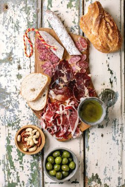 Geleneksel İspanyol jambonu Jamon Iberico, dilimlenmiş Fuet sosisi, yeşil zeytin, beyaz ekmek, fındık, zeytinyağı. Açık kırsal ahşap arkaplan, üst görünüm.