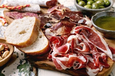 Snack board with traditional Spanish ham Jamon Iberico, sliced Fuet sausage, green olives, white bread, nuts, olive oil. Light rustic wooden table clipart