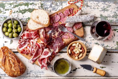 Geleneksel İspanyol Jamon Iberico, dilimlenmiş Fuet sosisi, peynir, yeşil zeytin, beyaz ekmek, fındık, zeytinyağı, bir bardak kırmızı şarap. Açık kırsal ahşap arkaplan, üst görünüm.