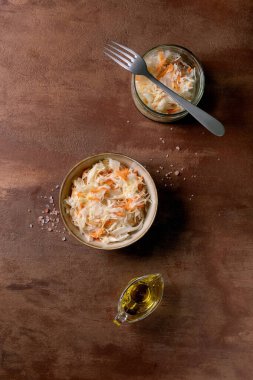 Geleneksel meze lahana turşusu ve havuç kasesi ve kavanozla birlikte. Deniz tuzu, zeytinyağı ve çatal yakında. Sağlıklı yiyecekler, mayalanmış ürünler. Kahverengi desenli arka plan. Üst görünüm