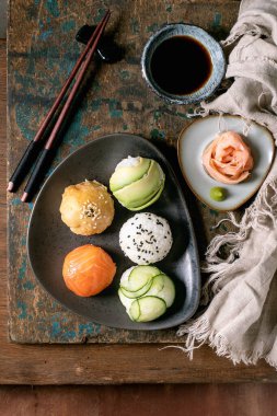 Temari suşi. Somon, avokado, salatalık ve Japon omleti ile kahverengi seramik tabakta moda suşi topları. Soya sosu, turşulu zencefil, yemek çubuğu, ahşap arka planda keten peçete. Üst görünüm.