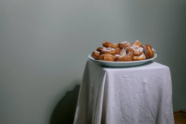 Mavi tabakta servis edilen toza bulanmış taze ev yapımı çörekler. Nötr arkaplana karşı beyaz masa örtüsü ile minimalist kompozisyon.