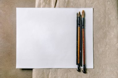 Boş beyaz kağıda yerleştirilmiş tahta saplı geleneksel boya fırçaları. Doğal Kraft pirinci ve dut kağıdı arkaplanı olan temiz sanat atölyesi yaratıcı süreç için hazır..