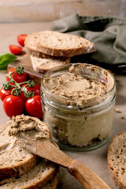 Cam kavanozda ev yapımı et ezmesi taze tahıllı ekmek dilimleri kiraz domatesleri ve fesleğen yapraklarıyla servis ediliyor. Kırsal tahta kaşık ve kesme tahtası.