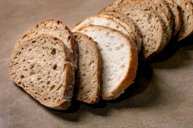 Kahverengi arka planda karışık beyaz ve kahverengi parçalarla dilimlenmiş zanaatkar ekmeği. Yumuşak doku ve kabuğu gösteren taze ev yapımı ekmek..