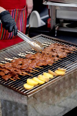 Siyah eldivenli, rengarenk önlüklü, marine edilmiş et şişleri ve sokak yemeği ızgarasında patates dilimleri yapan bir aşçı. Restoran pişirme işlemi.