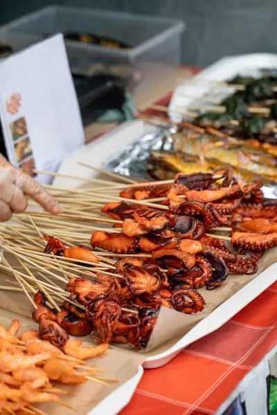 Ahşap çubuklarda taze ızgara ahtapot şiş sokak gıda pazarında sergileniyor. Deniz ürünleri lezzeti geleneksel Asya stili hazırladı. Seçime el işareti.