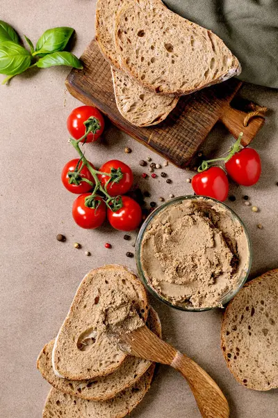 Ev yapımı mayalı ekmek dilimleri karaciğer ezmesi taze kiraz domatesleri fesleğen yaprakları ve ahşap kesim tahtasında baharatlar. Kırsal kahvaltı seti.