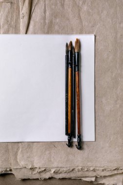 Beyaz pirinç ve dut kâğıdının üzerine yerleştirilmiş ahşap saplı ve doğal kıllı üç geleneksel hat fırçası ve dokulu kraft kağıdına karşı dut kağıdı..