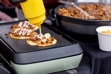 Mini tacolara kıymalı sos ekleyen şefe yakın çekim. Biftek pişirirken ev yapımı takoların üzerine serpiştirilmiş kremalı sos. Yakınlarda et dolu demir tava dökün..