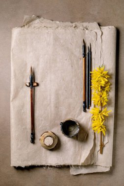 Klasik hat sanatı fırçaları mürekkep kabı ve el yapımı dut kağıdı arka planda sarı forsythia çiçekleri. Yaratıcı çalışma alanı için sanatsal düz konum.