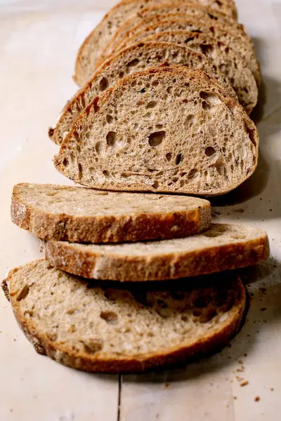 Köy ekmeği dilimleri, gözenekli dokular ve ahşap zemin üzerinde çıtır çıtır çıtır. Kahvaltı ya da sandviç için mükemmel bir ekşi ekmek yakın plan..