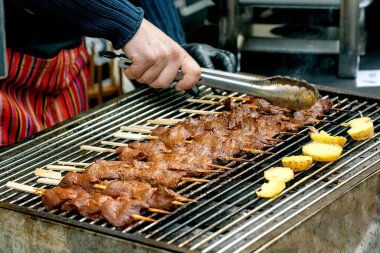 Şef mangalda et şiş ve patates pişiriyor. Sokak yemekleri festivalinde geleneksel kebapları hazırlayan maşalar. Açık hava pişirme işlemi.