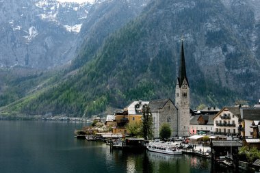 Avusturya 'daki görkemli Alpler dağlarıyla çevrili tarihi kilise binalarıyla Hallstatt köyünün manzarası. Turist teknesi ahşap iskeleye yanaştı..
