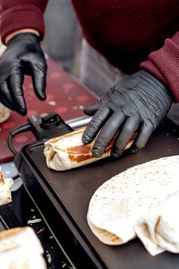 Siyah eldivenli şef sıcak ızgara üzerine burrito hazırlıyor. Tortilla ambalajını sokak yemekhanesinde dolduran ellerin yakın görüntüsü.