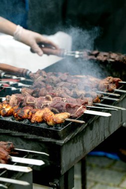 Barbeküde ızgara et şişi yapan kişi. Tavuk ve biftek parçaları ile sulu kebaplar kızgın ızgaradan yükselen dumanlı metal şişler üzerinde pişiyor..
