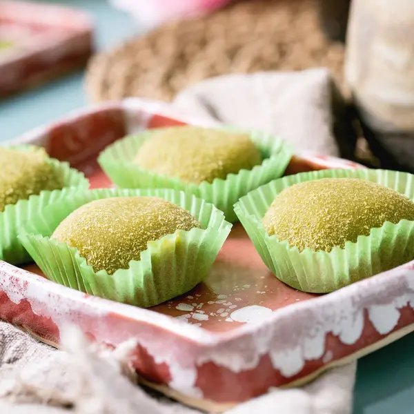 Geleneksel Asya pirinç tatlısına yakın yeşil kibrit mochi pembe seramik tabakta mavi masada..