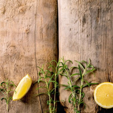 Citrus ve şifalı bitkiler. Eski ahşap arka planda taze organik dilimlenmiş limon ve biberiye dalları. Üst görünüm, alanı kopyala