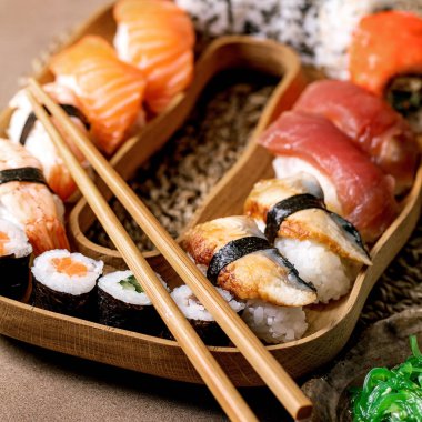 Suşi hazır. Geleneksel Japon yemeği suşisi ve taze somon, ton balığı, yılan balığı ve pirinçli karides. Kahverengi masadaki ahşap tabakta servis. Kapat.