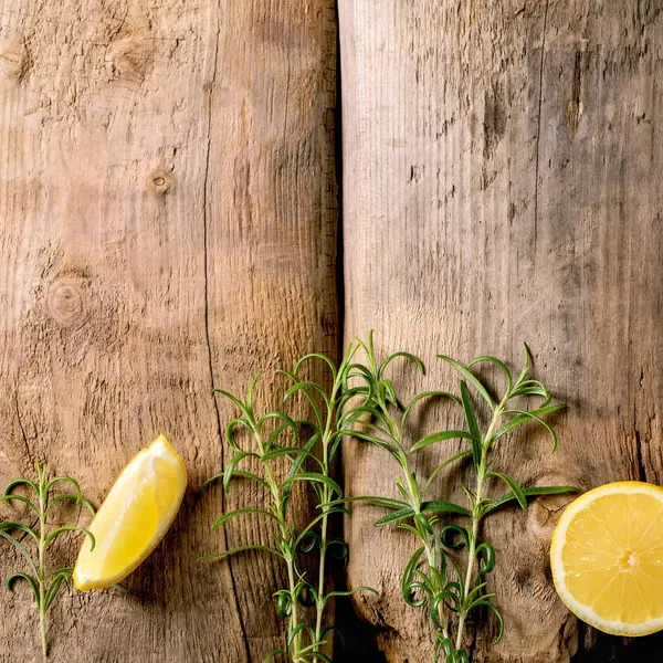 Citrus ve şifalı bitkiler. Eski ahşap arka planda taze organik dilimlenmiş limon ve biberiye dalları. Üst görünüm, alanı kopyala