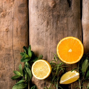 Citrus ve şifalı bitkiler. Taze organik dilimlenmiş limon, nane ve biberiye dallarıyla eski ahşap zemin üzerinde portakal. Üst görünüm, alanı kopyala