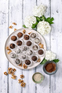 Ev yapımı çikolatalı çiğ vejetaryen enerji topları ya da kakao tozu susam tohumlu mantarlar ve beyaz ahşap arka planda ortanca çiçekli cevizler.