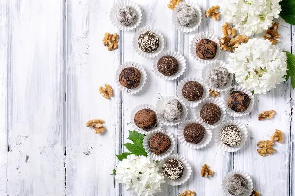 Ev yapımı çikolatalı çiğ vejetaryen toplar değişik kaplamalı mantar çeşitleri ceviz ve kırsal beyaz ahşap arka planda beyaz ortanca çiçekleri.