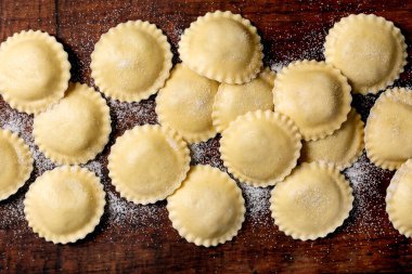 Un ahşap kesme tahtasının üzerinde el yapımı ravioli makarna. Geleneksel İtalyan yemekleri pişmeye hazır çiğ hamur köftelerini gösteriyor..