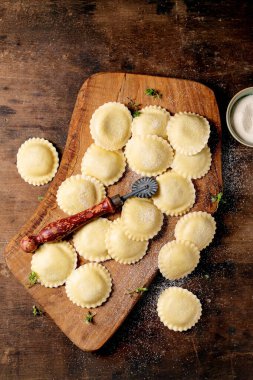 Kaba ahşap kesme tahtasının üzerinde ev yapımı ravioli makarna. Koyu ahşap arka planda un tozuyla kaplanmış makarna.